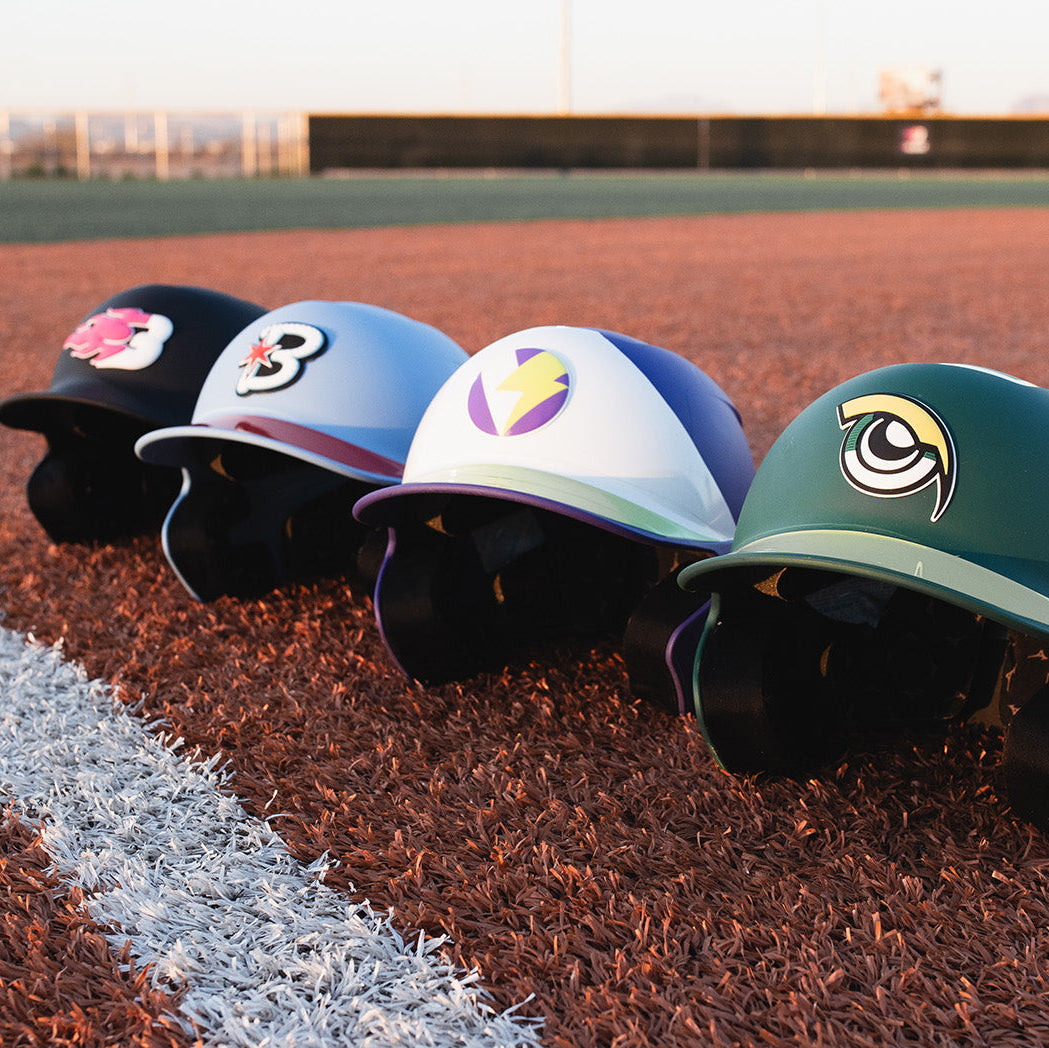 Four baseball helmets with colorful designs on a baseball field