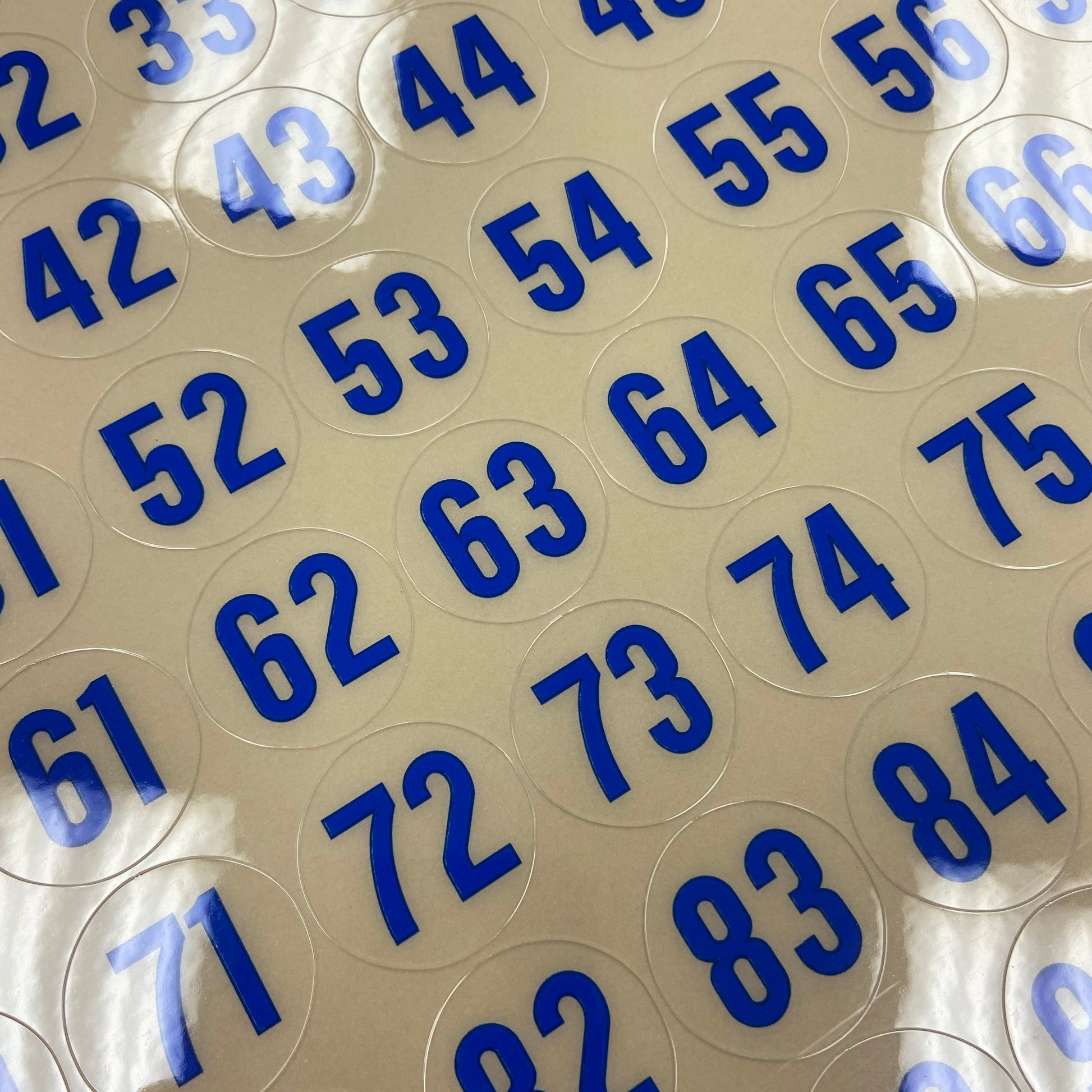 Close-up of round transparent stickers with blue numbers on a beige background
