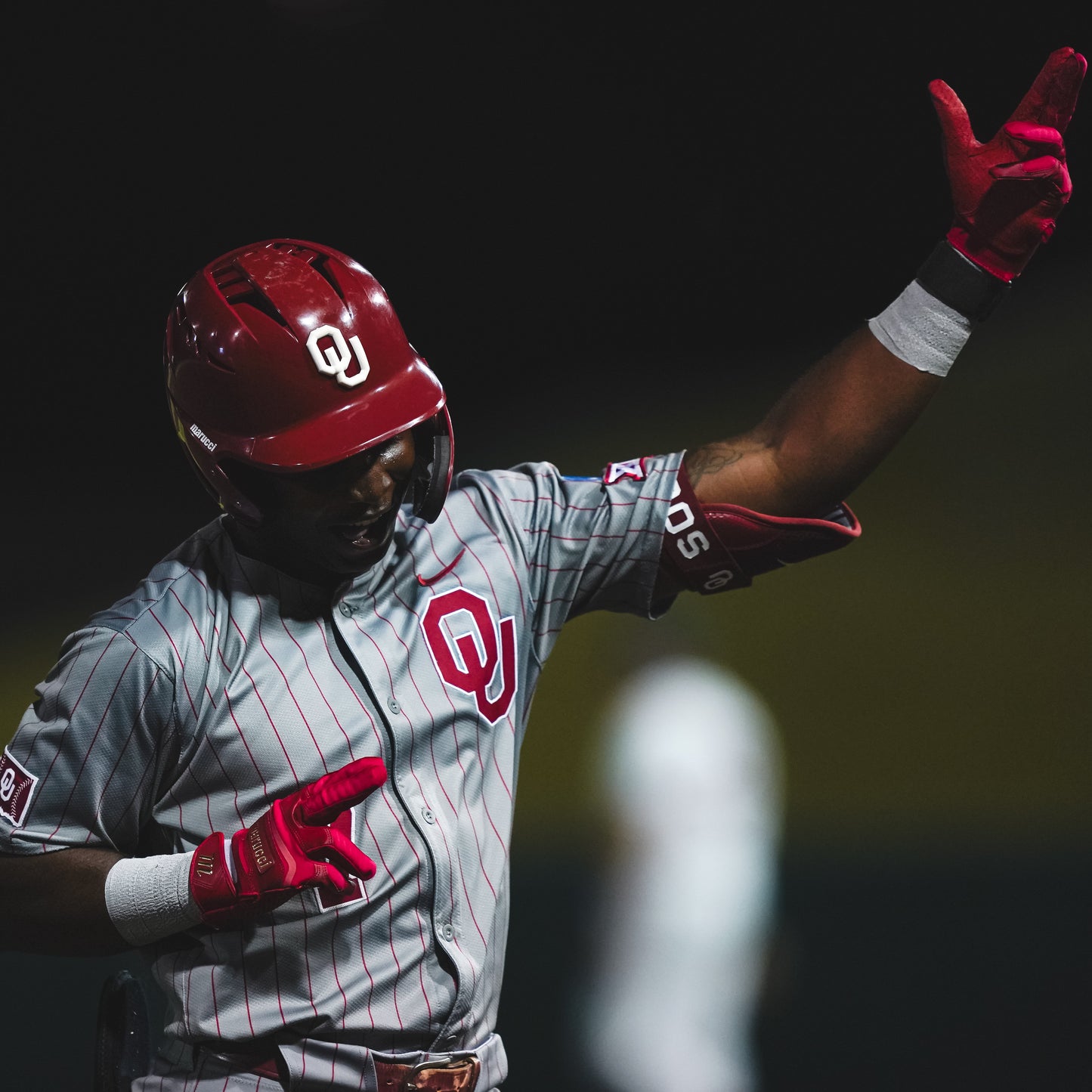 Baseball player in a gray and red uniform with 'O' logo, wearing red helmet and gloves, on a dark background.