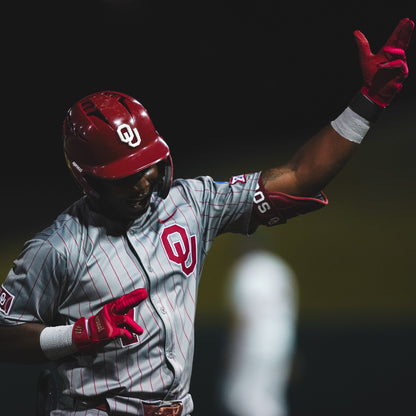 Baseball player in a gray and red uniform with 'O' logo, wearing red helmet and gloves, on a dark background.